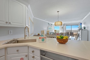 A kitchen with a white countertop, a wooden bowl of fruit, and a hanging light fixture. - Direct Beachfront 2BR Condo w Ocean Views & Private Pool (Hilton Head Island)