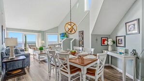 A spacious living room with a dining area, large windows, and a view of the ocean.
