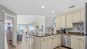 A modern kitchen with light-colored cabinets, a stainless steel dishwasher, and a granite countertop.