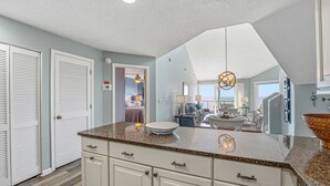 A spacious kitchen with a granite countertop, white cabinetry, and a hanging light fixture.