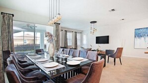 Un comedor moderno con una mesa larga dispuesta para seis comensales, rodeada de sillas cómodas. Un amplio ventanal ofrece vistas al exterior, y un televisor de pantalla plana está montado en la pared.