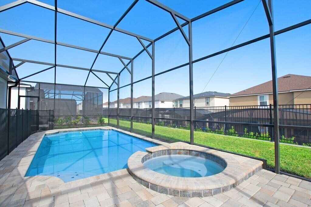 A backyard with a swimming pool and hot tub, enclosed by a metal fence.
