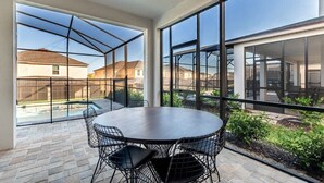 Un patio moderno con una mesa redonda y sillas, ventanas amplias y vista a una zona residencial.