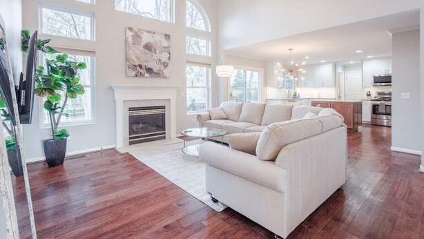A spacious living room with a fireplace, large windows, and a modern kitchen in the background.