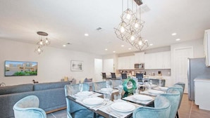 A modern dining area with a long table set for six, light blue upholstered chairs, and contemporary pendant lighting.