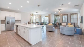 A spacious kitchen with white cabinets and a central island, a living area with a sofa and chairs, and a dining area with a table and chairs.