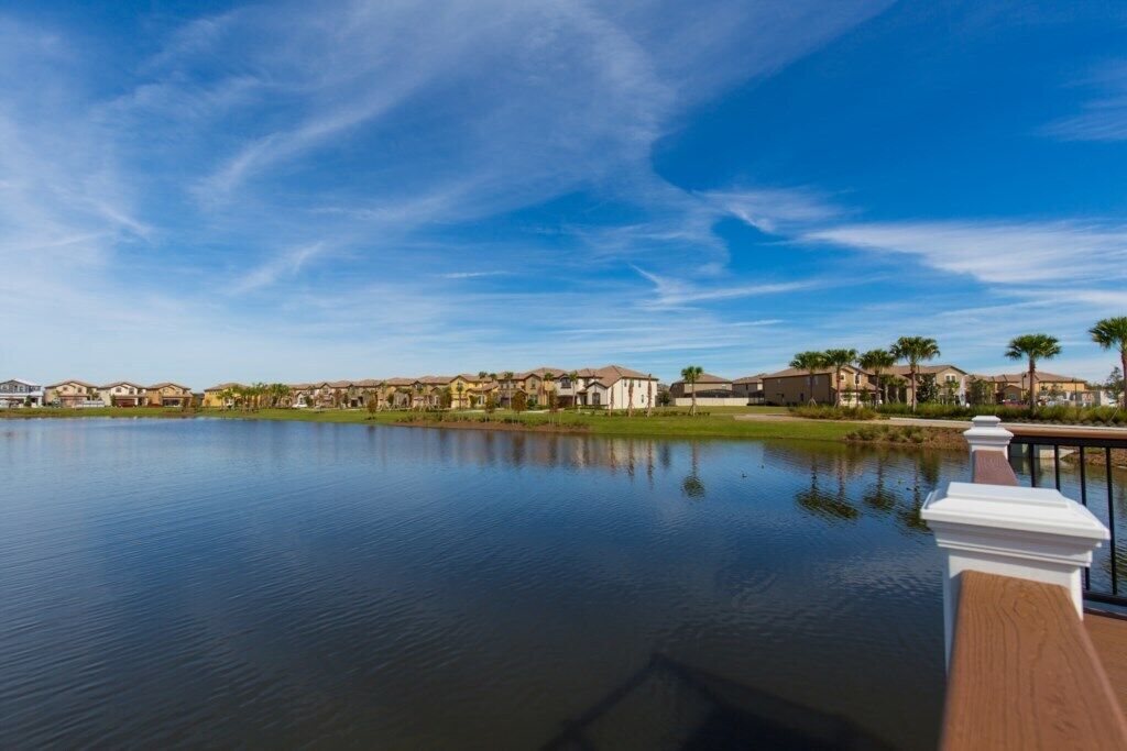 A tranquil lakeside view with a wooden deck and a row of houses in the background.