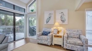 Una habitación con dos sillones estampados, una mesita de noche con lámpara y dos cuadros de pájaros colgados en la pared.