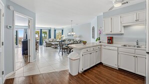 A modern kitchen with white cabinets, a central island, and a dining area with a table and chairs. - Oceanfront Villa | Direct Beach Access, Private Pool, King Suite & Ocean Views (Hilton Head Island)