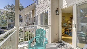 A balcony with a turquoise chair, a white railing, and a view of a neighboring building. - Forest Beach Villa | Sleeps 6 | Walk to Coligny Plaza, Beach & Dining (Hilton Head Island)