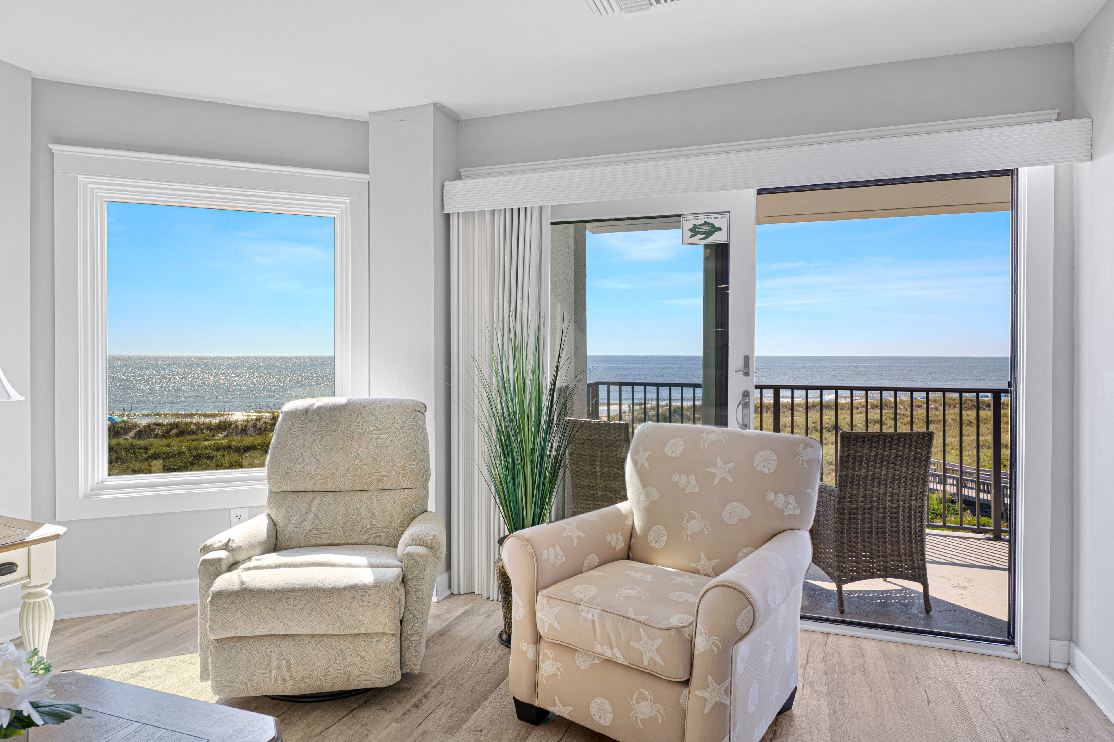 Een balkon met twee stoelen, uitzicht op zee, en een bord met informatie over zeeschildpadden.