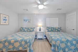This spacious guest bedroom offers two beautifully appointed beds with matching white wood frames and coastal-inspired bedding.