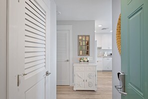 A hallway with a white door, a white cabinet with decorative shells, and a green door.