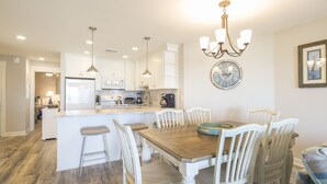 Una cocina moderna con muebles blancos, una isla central y una zona de comedor con sillas blancas.