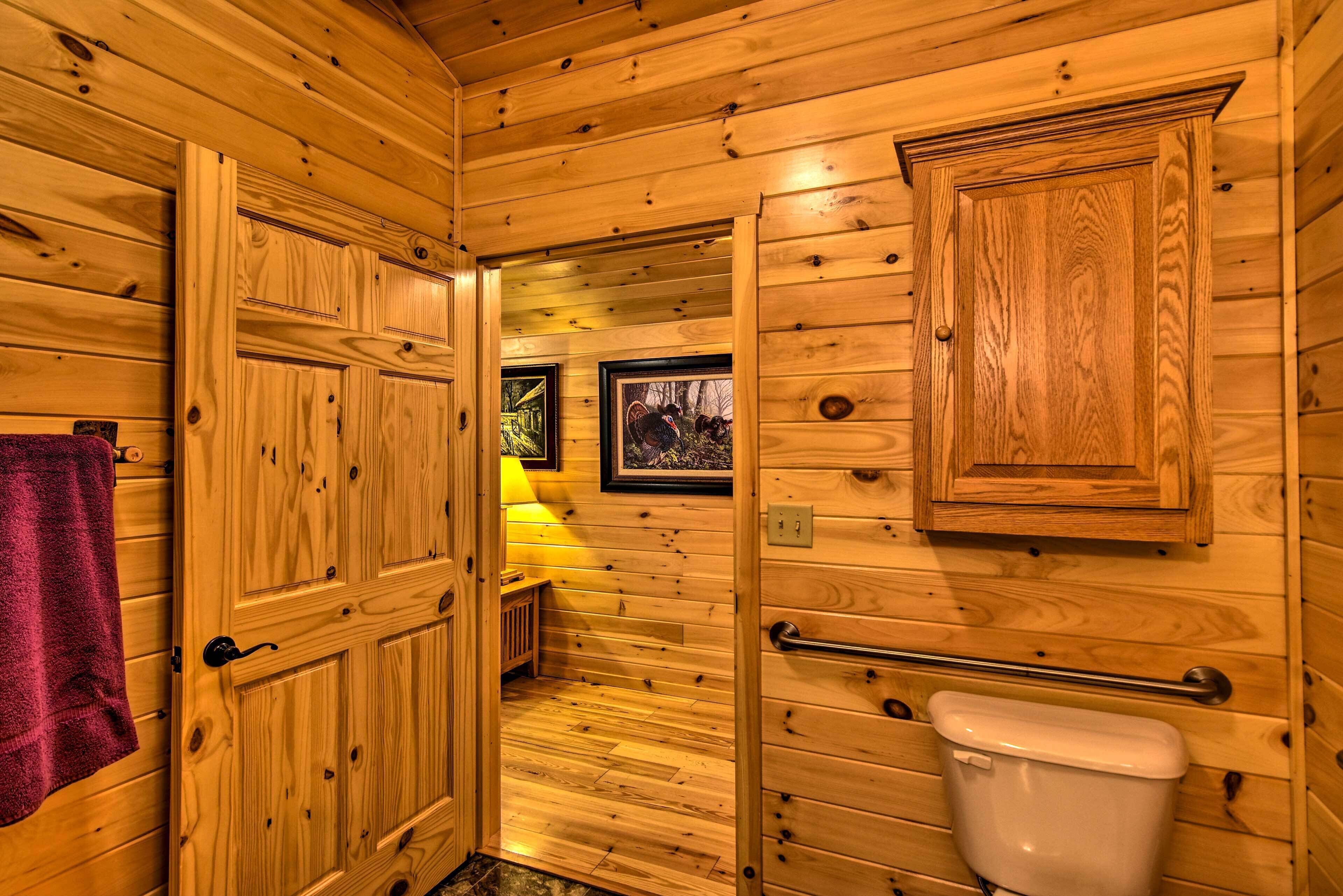 Interior de una cabaña de madera con puerta de madera, un inodoro, un pequeño banco y cuadros en la pared.
