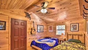 A wooden cabin bedroom with a bed, a guitar, and framed pictures on the walls.
