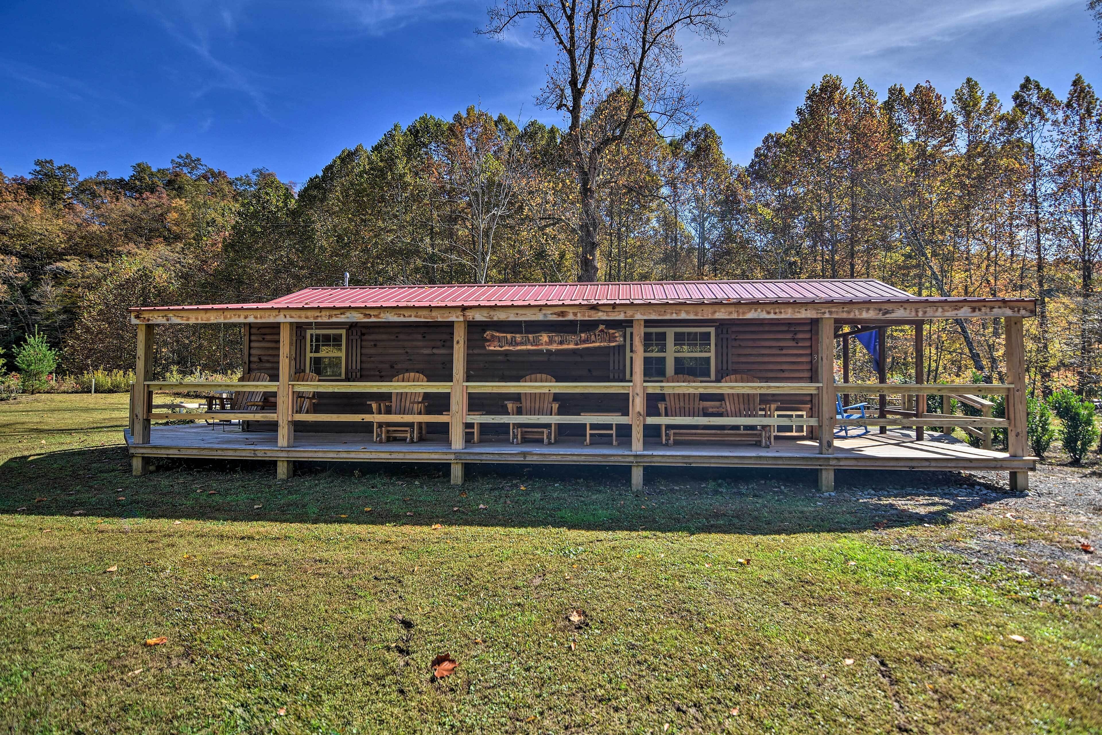A rustic cabin with a covered porch and outdoor seating area, surrounded by trees.