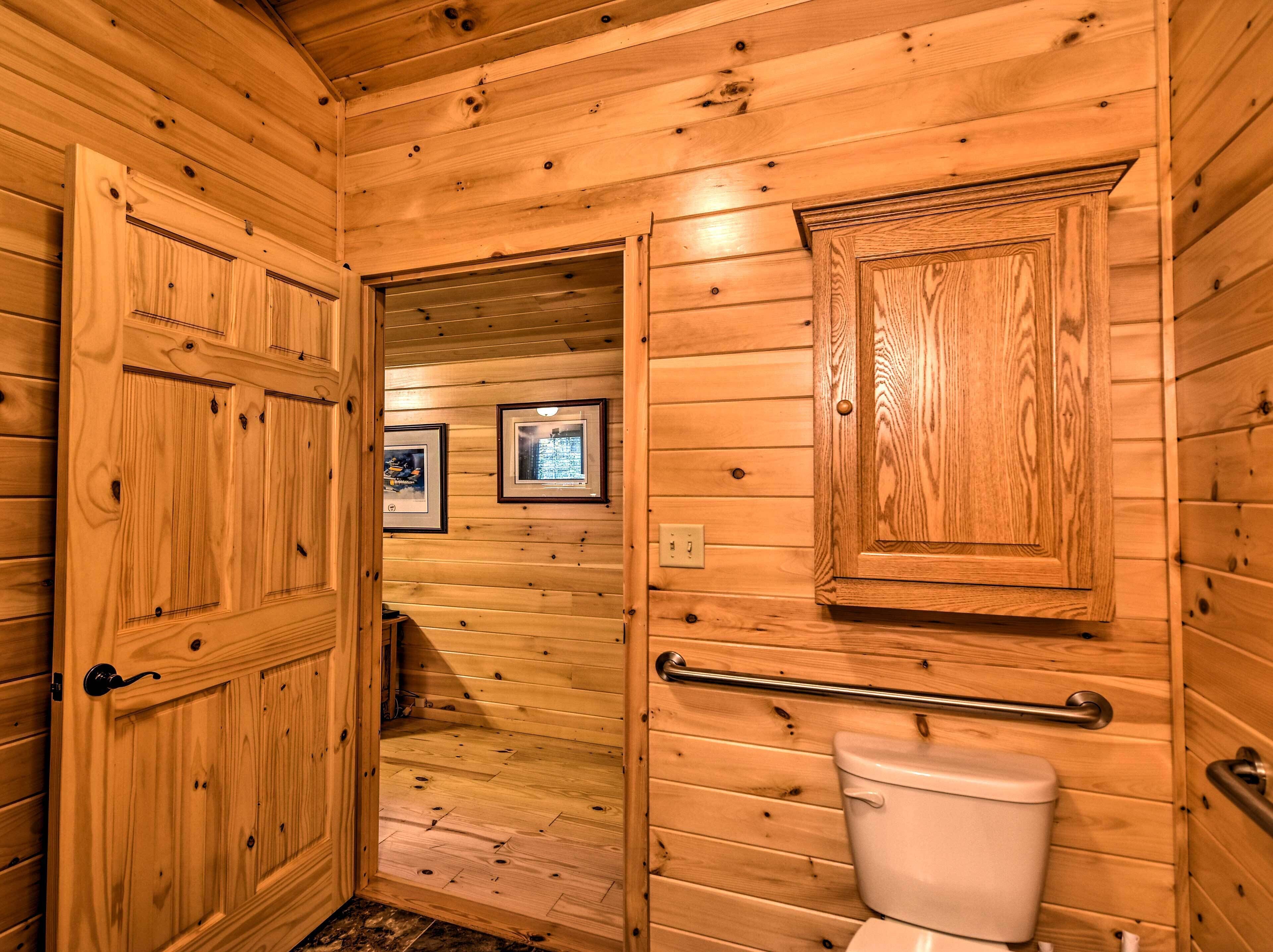 A wooden-paneled bathroom with a toilet, a handrail, and framed pictures on the wall.