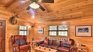 A wooden cabin interior with a leather armchair, a leather sofa, a wooden coffee table, and a ceiling fan.