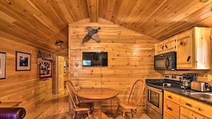 A wooden interior with a dining table, chairs, a fireplace, wooden cabinets, and a television.