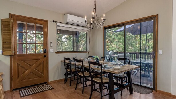 A dining area with a wooden table and chairs, large windows, and a view of the outdoors.