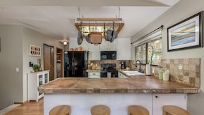 A modern kitchen with a central island, bar stools, hanging pots, and a large window.