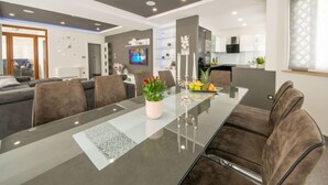 Ein modernes Wohnzimmer mit einem Glastisch, Ledersesseln, einer Couch und einem Fernseher im Hintergrund.
