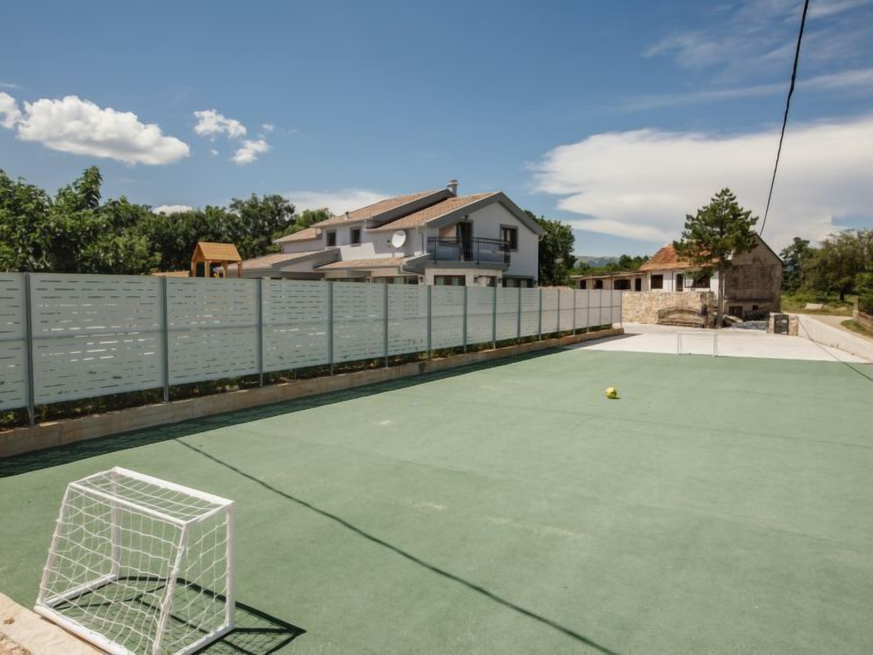 A sports court with a goalpost, surrounded by a fence and houses in the background.