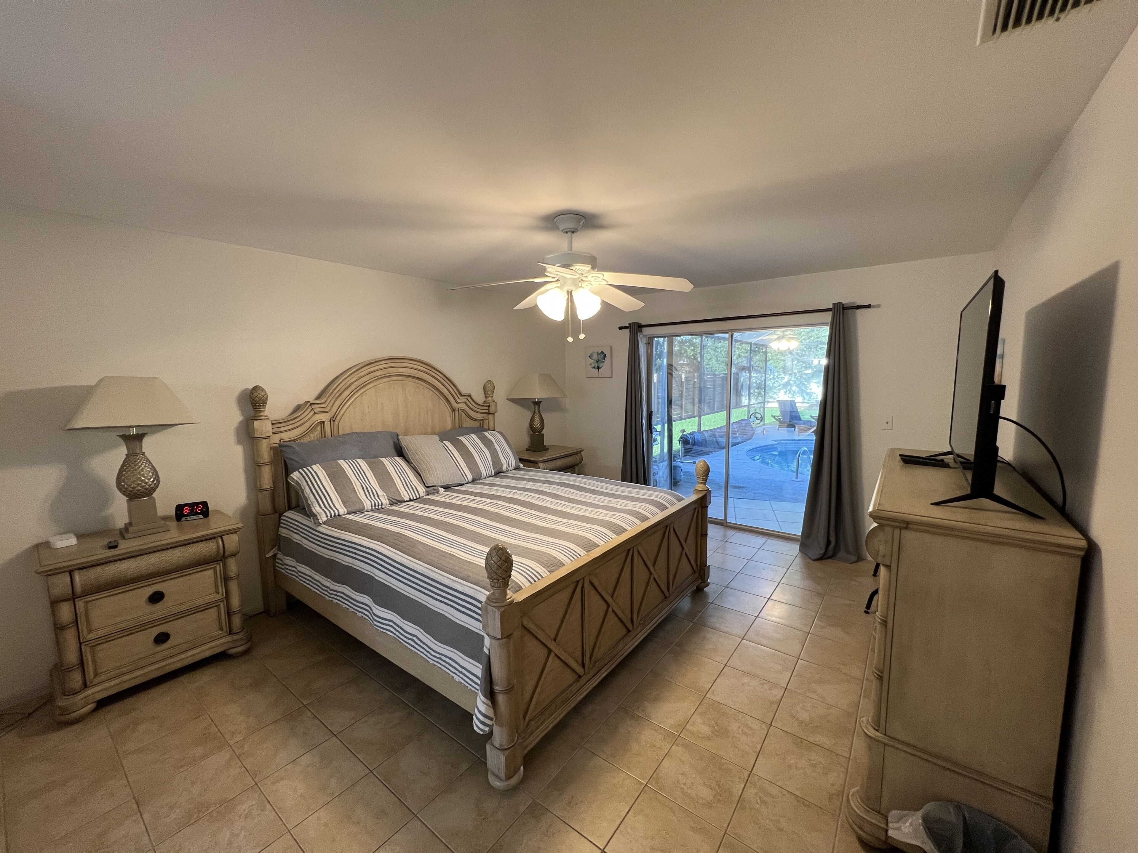 Un dormitorio con cama, mesitas de noche, televisor y puerta corrediza de cristal a un patio.