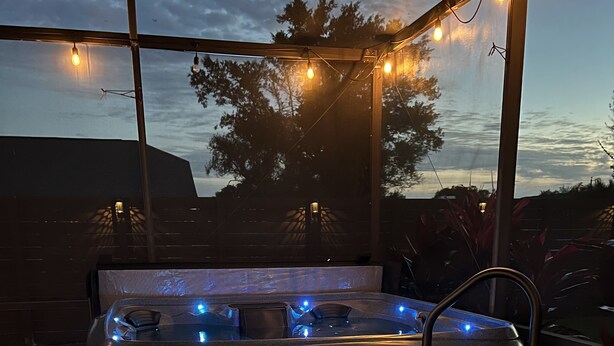 Ein Whirlpool mit LED-Beleuchtung, ein Fliesenboden aus Stein und im Hintergrund Bäume sowie ein Gebäude.