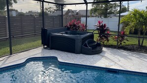 Ein Whirlpool in einem überdachten Außenbereich mit Pool, umgeben von Pflanzen und Blick auf eine Wohngegend.