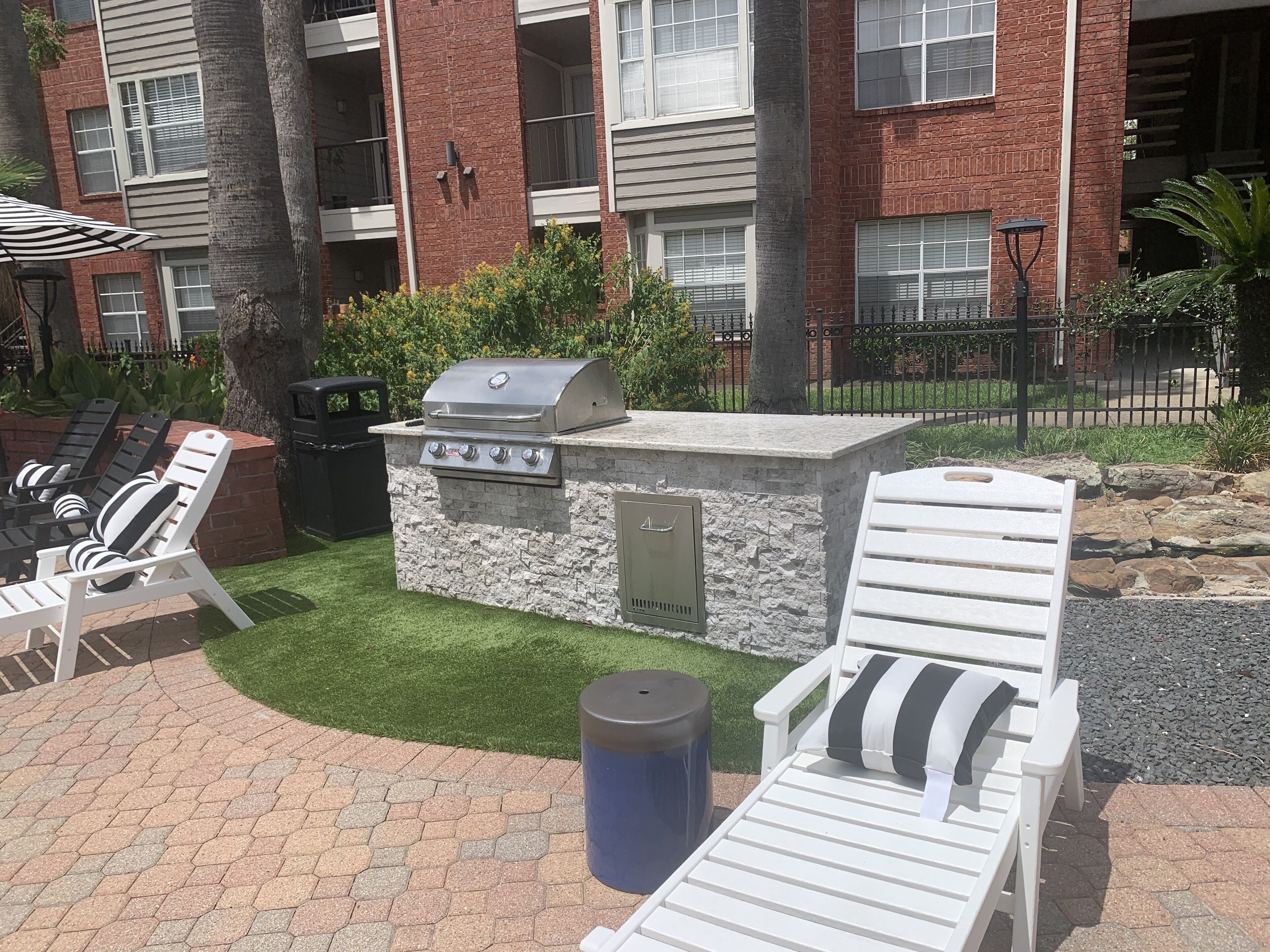 An outdoor patio with a barbecue grill, lounge chairs, and a trash can.