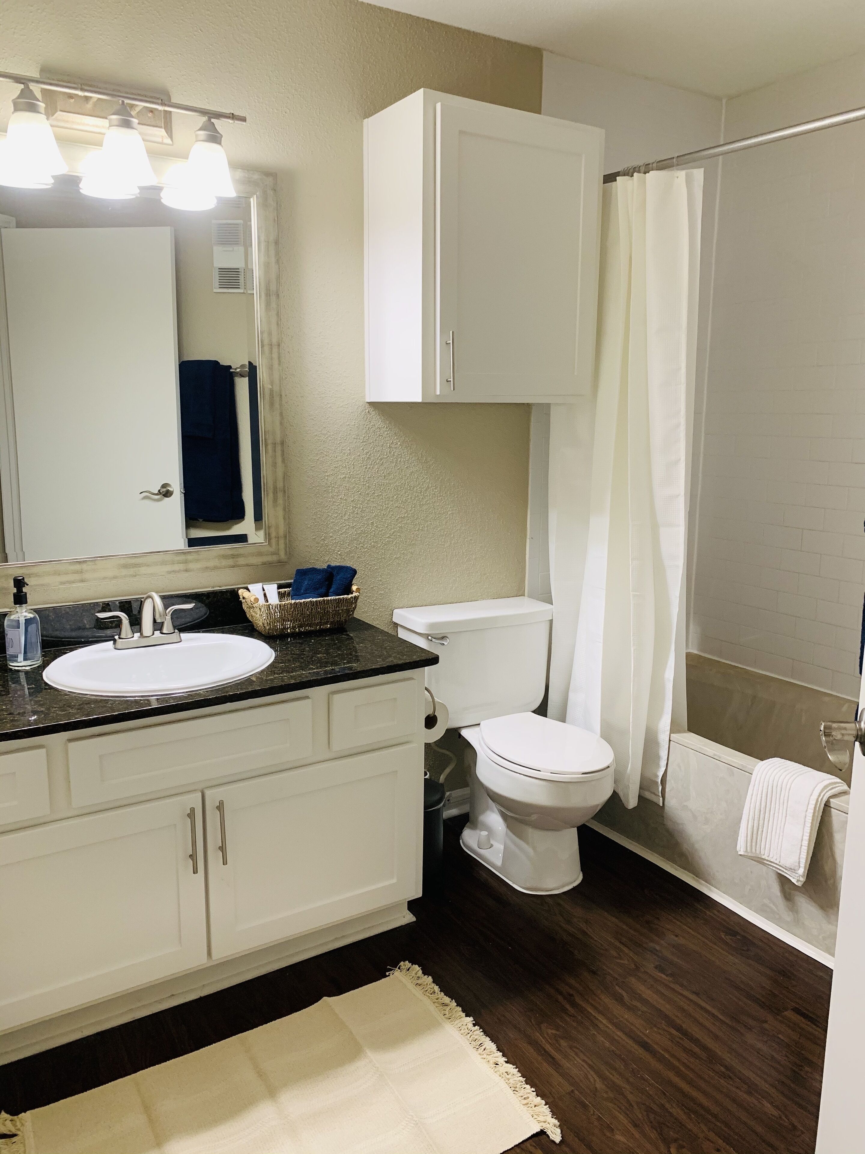A bathroom with a white sink, a toilet, a shower curtain, and a mirror with lights.