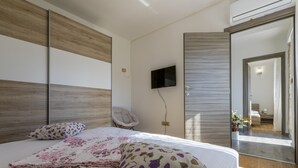 A modern bedroom with a large bed, a flat-screen TV, a chair, and a door leading to another room. - Villa Odiseja (Tribalj)