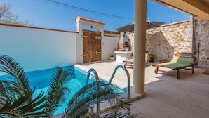 A pool area with a wooden door, a stone wall, and a lounge chair. - Villa Odiseja (Tribalj)