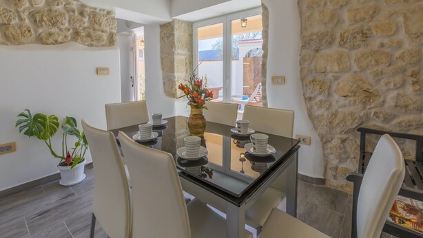 A dining area with a glass table, white chairs, and a vase with flowers. - Villa Odiseja (Tribalj)