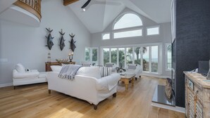 A spacious living room with a white sofa, a wooden coffee table, and a view of the ocean through large windows. - Luxury Family Oceanfront Oasis | Private Pool, Sun Decks w Views, Walkable to Coligny Plaza (Hilton Head Island)