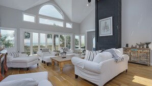 A spacious living room with white furniture, large windows, and a view of the ocean. - Luxury Family Oceanfront Oasis | Private Pool, Sun Decks w Views, Walkable to Coligny Plaza (Hilton Head Island)