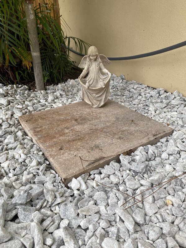 A statue of a figure with wings on a stone platform surrounded by white pebbles.