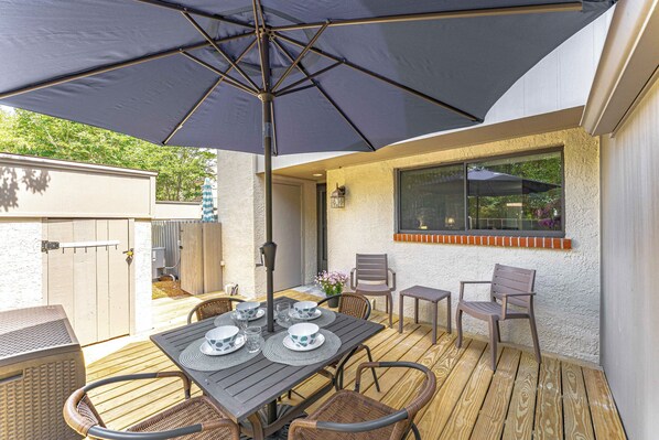 An outdoor patio with a table set for dining, surrounded by wicker chairs, under a large umbrella.