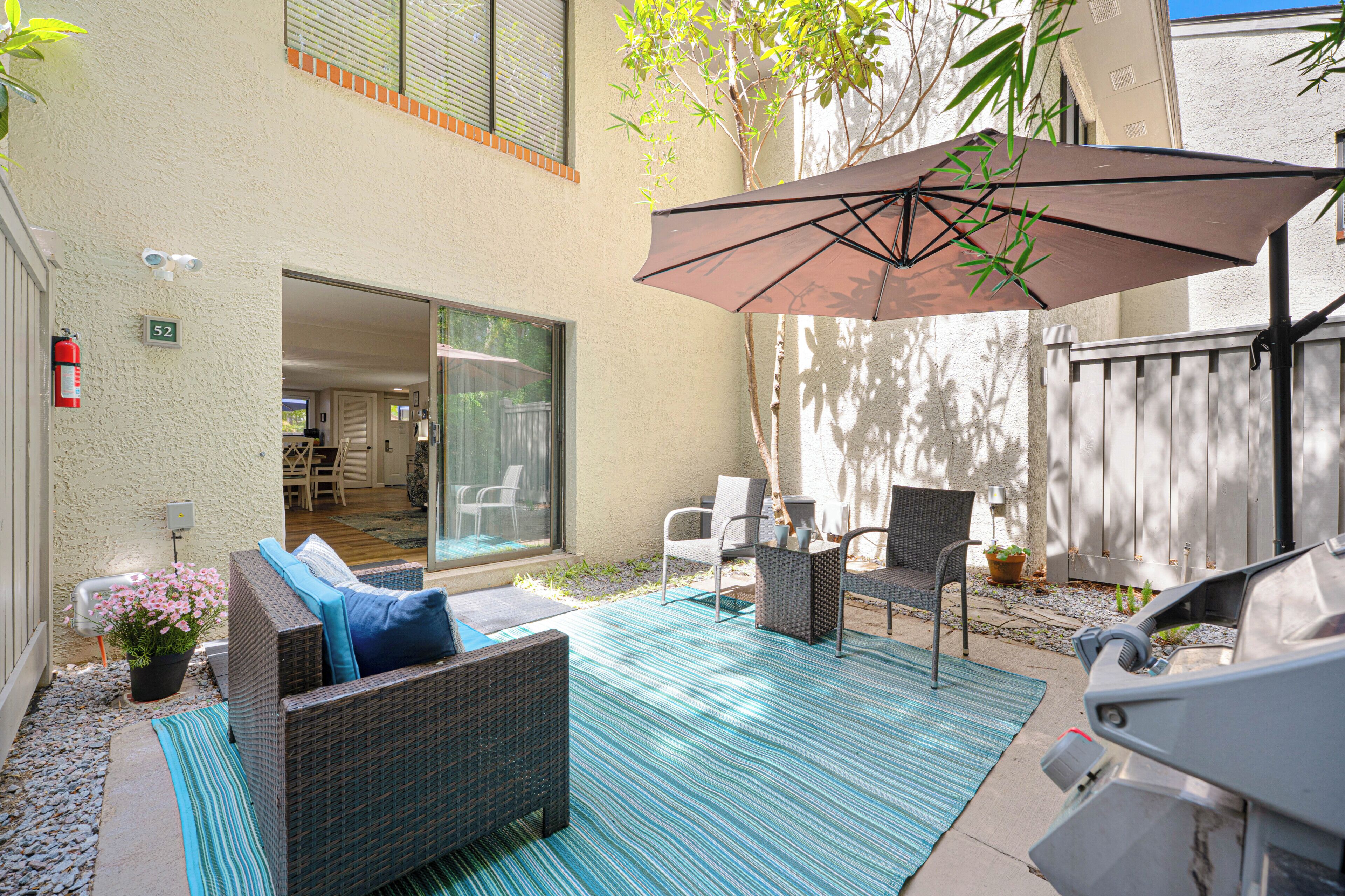 A patio with wicker furniture, a large umbrella, and a view of the interior through a glass door.