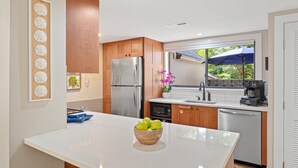 Una cocina moderna con una isla central, armarios de madera y electrodomésticos de acero inoxidable, y vistas al exterior.