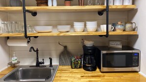 Une cuisine avec des étagères en bois où sont rangés de la vaisselle, une machine à café et un four à micro-ondes.