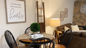 Un coin repas avec une table ronde, quatre chaises, une petite plante en pot et un panneau encadré accroché au mur.