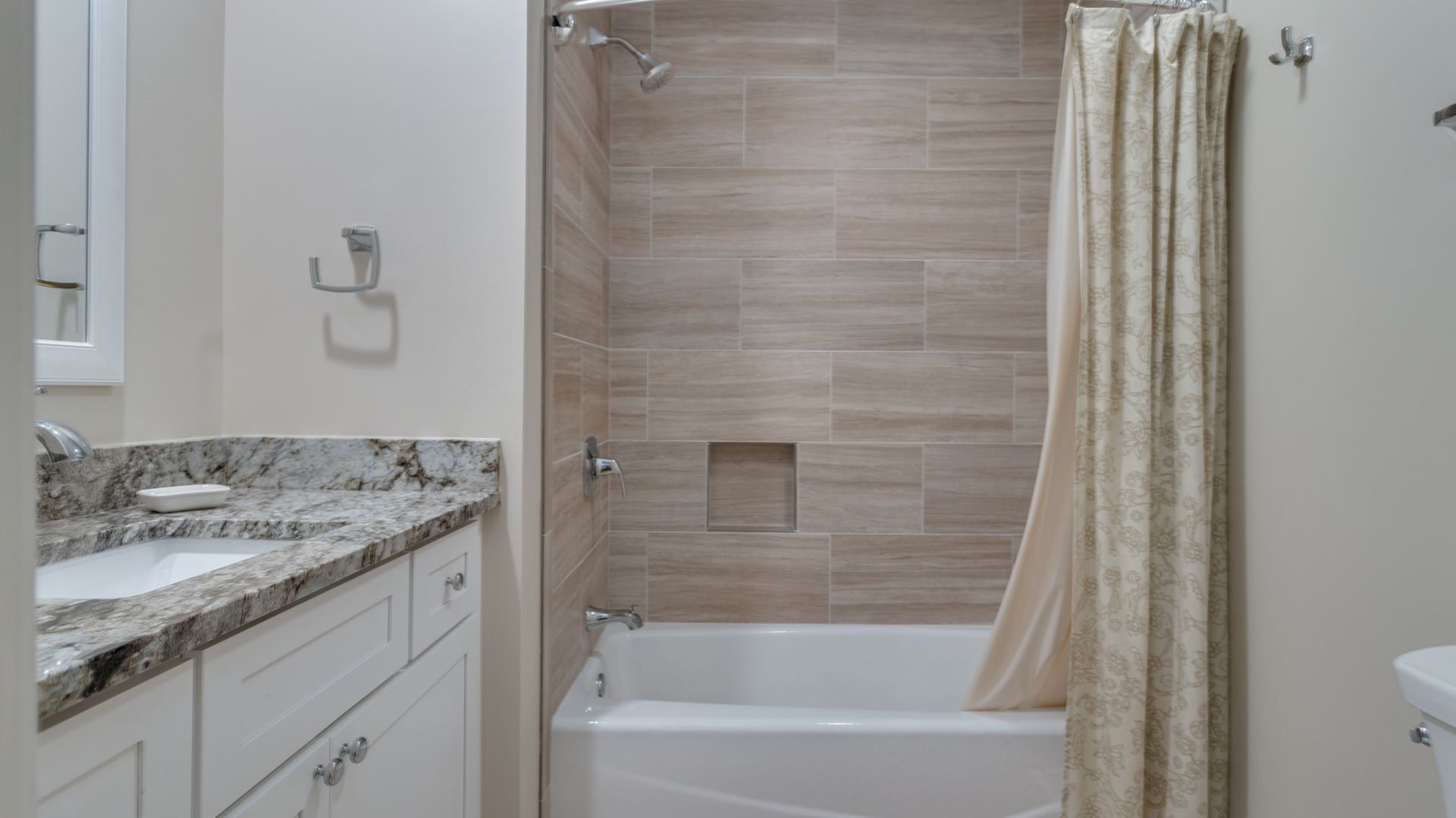 Un baño con encimera de mármol, bañera y paredes con azulejos color crema.