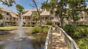 A multi-story hotel with a central courtyard featuring a water fountain, surrounded by lush greenery and trees. - Renovated Forest Beach Villa | Walk to Beach & Coligny Plaza (Hilton Head Island)