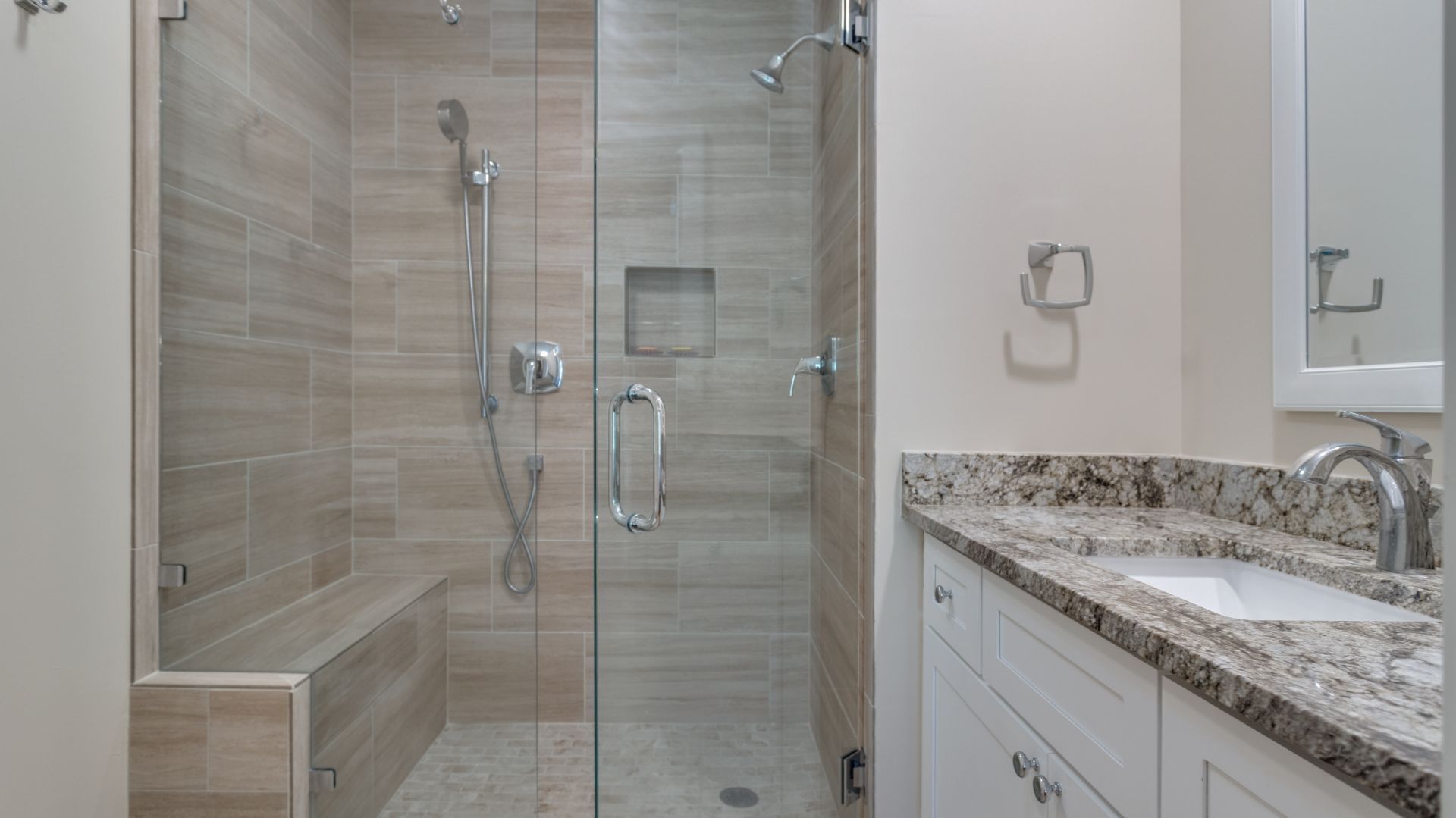 Ein modernes Badezimmer mit einer Glaskabine zur Dusche, einem Waschbecken auf einer Granitplatte und einer weißen Waschtischunterschrank.