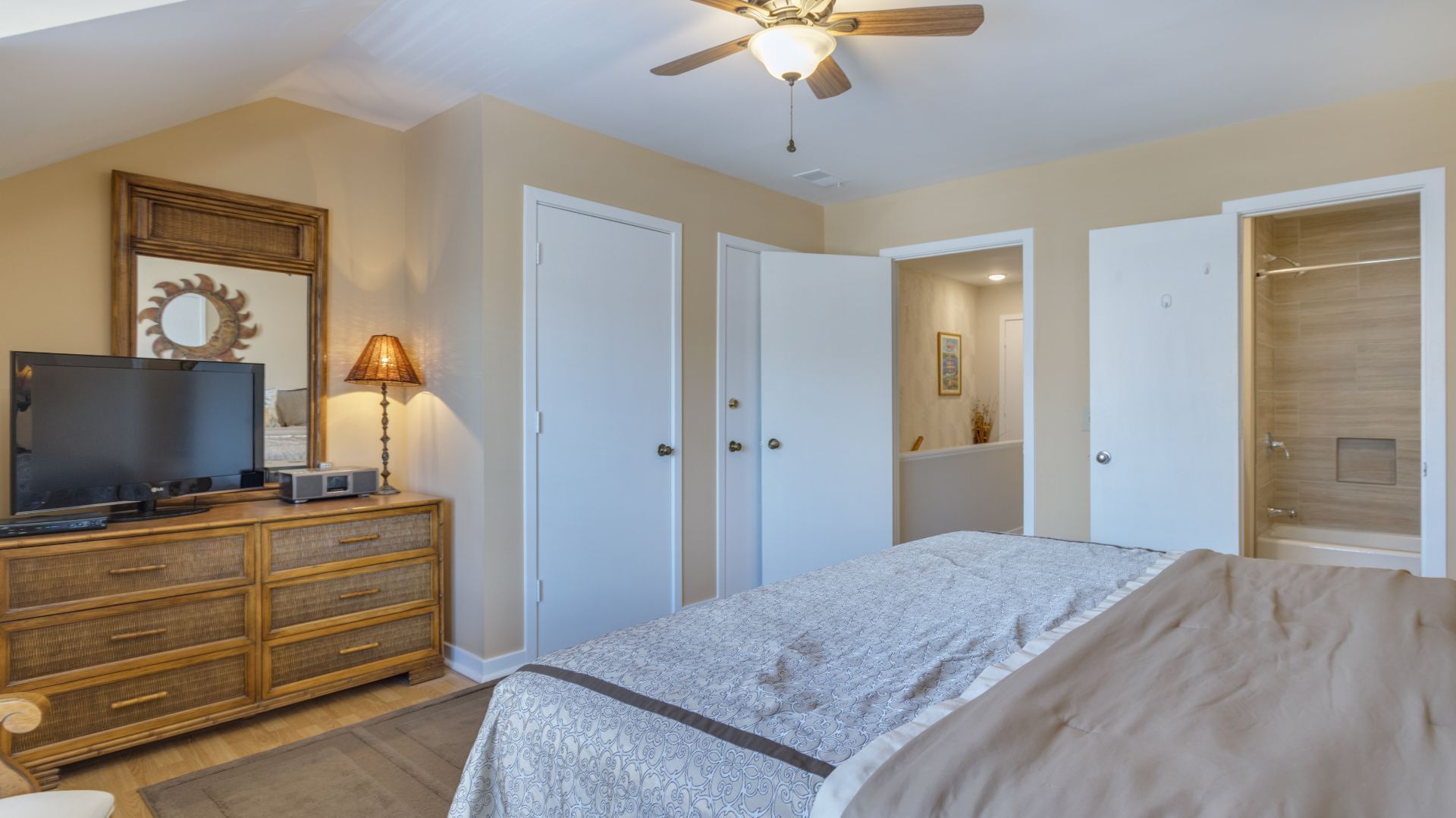A bedroom with a bed, a dresser, a television, and a ceiling fan.