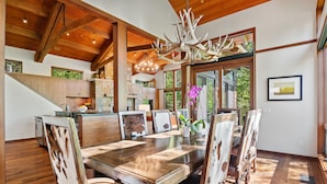 A spacious dining area with a large wooden table and chairs, a chandelier, and a view of the outdoors.