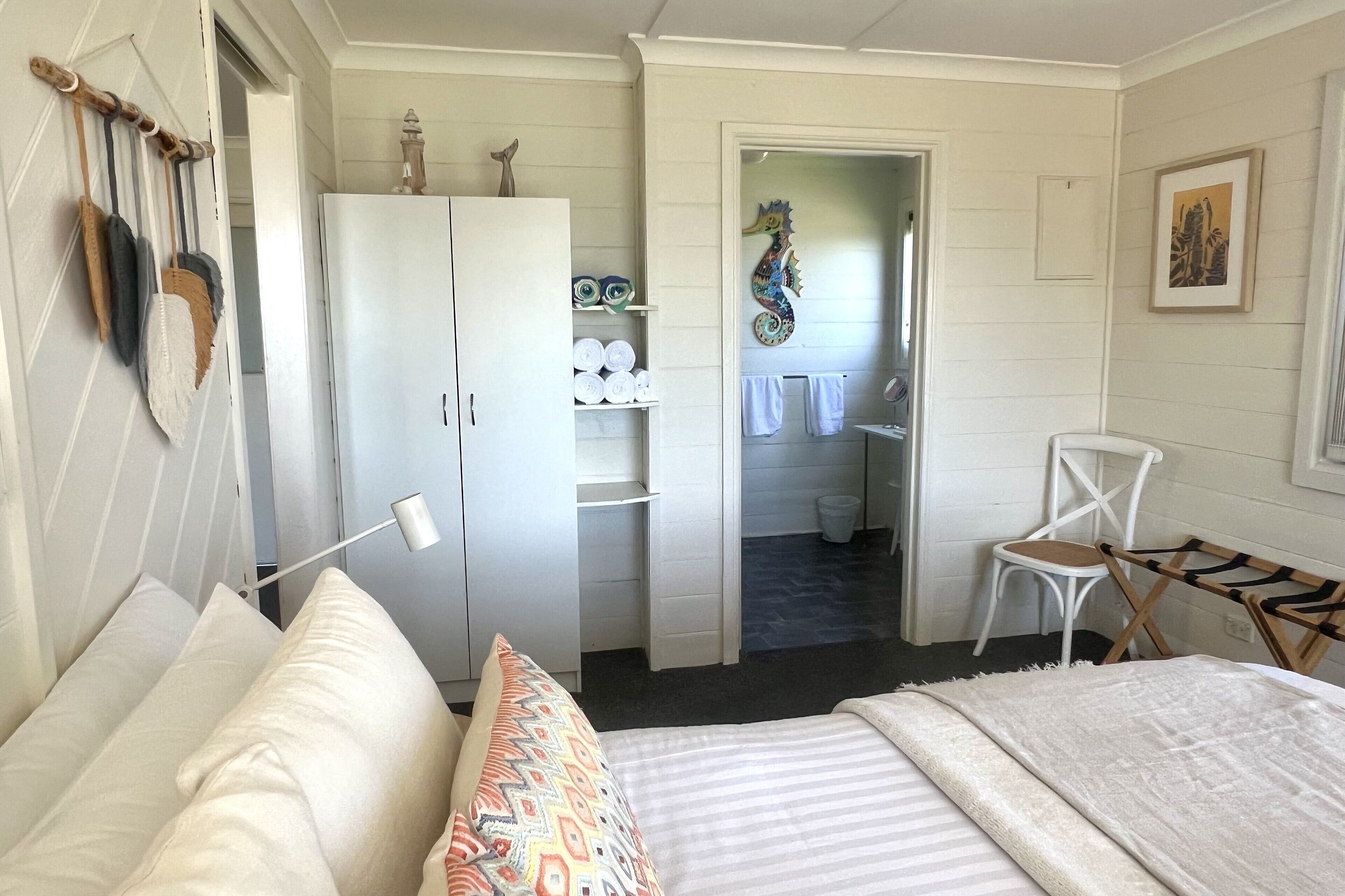 Un dormitorio con cama, armario, silla y baño visible a través de una puerta abierta.